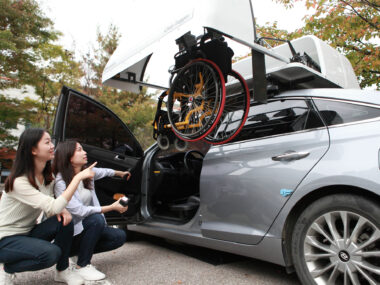 주차장에서 차량용(휠체어 적재용) 보조공학기기의 시연을 보고 있는 사람들의 모습