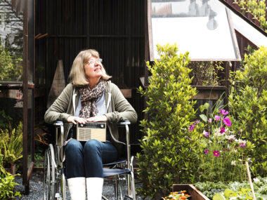 휠체어를 탄 여성이 푸릇푸릇한 식물원에서 미소를 짓는 사진