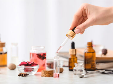 여러 개의 갈색 공병이 놓여져 있고, 여성의 손이 투명 공병에 향료를 배합하는 사진